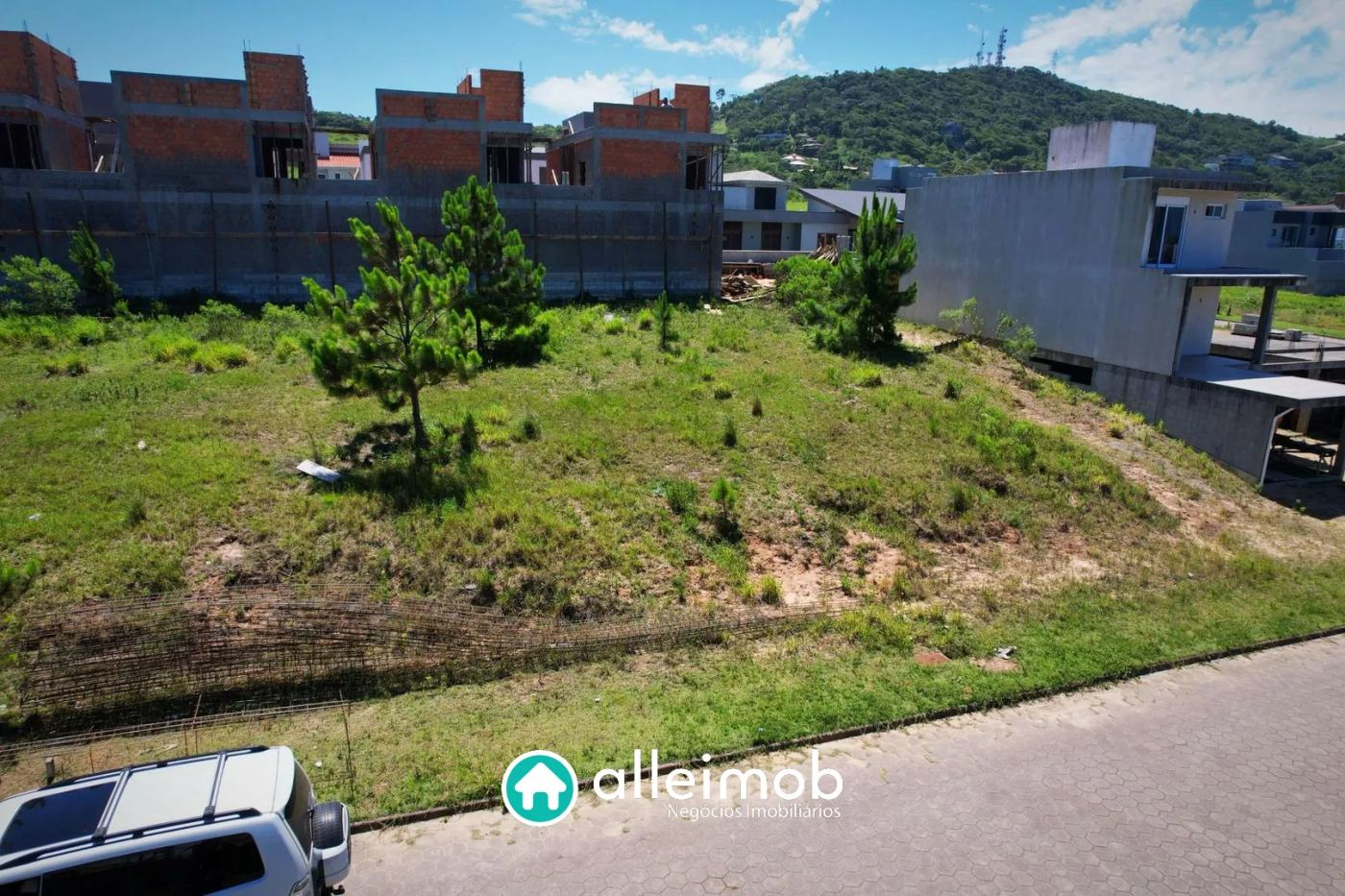 Terreno gramado em aclive numa rua de casas novas em Garopaba